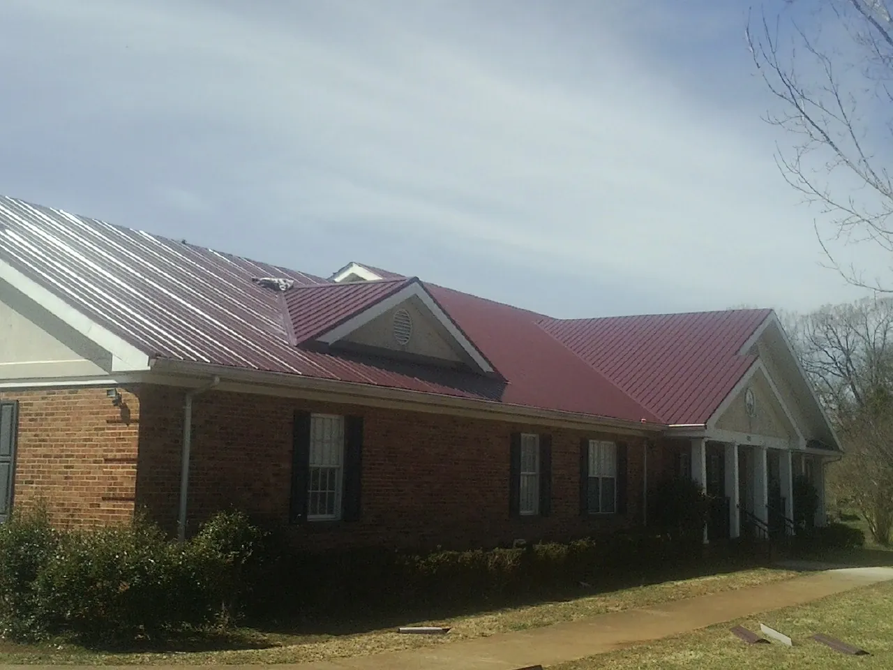 Red metal roof with gabled entries on a long brick building, from a Hail Damage Roof Repair job in Walla Walla