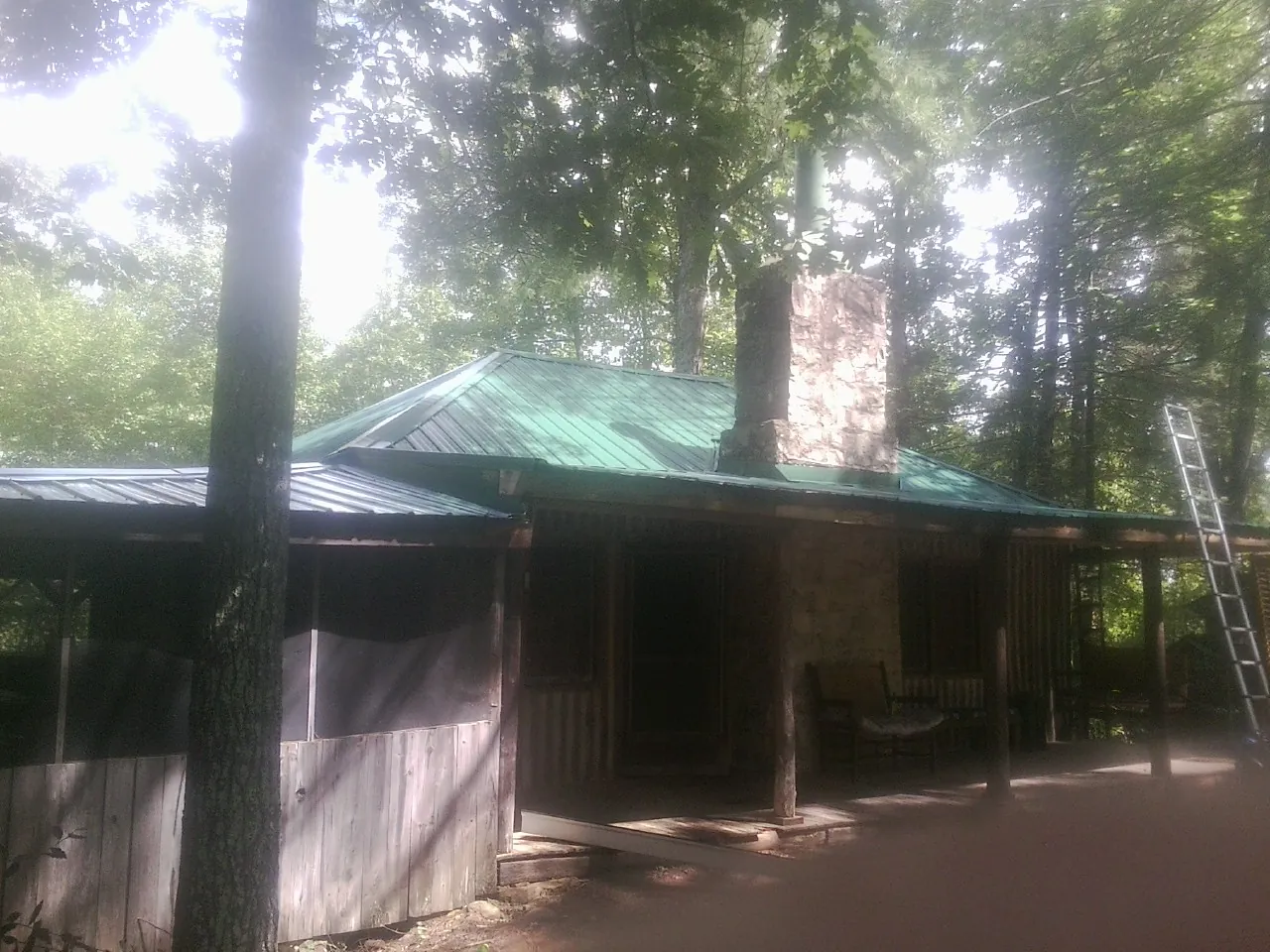 Green metal roof and stone chimney above a log cabin porch in Walla Walla