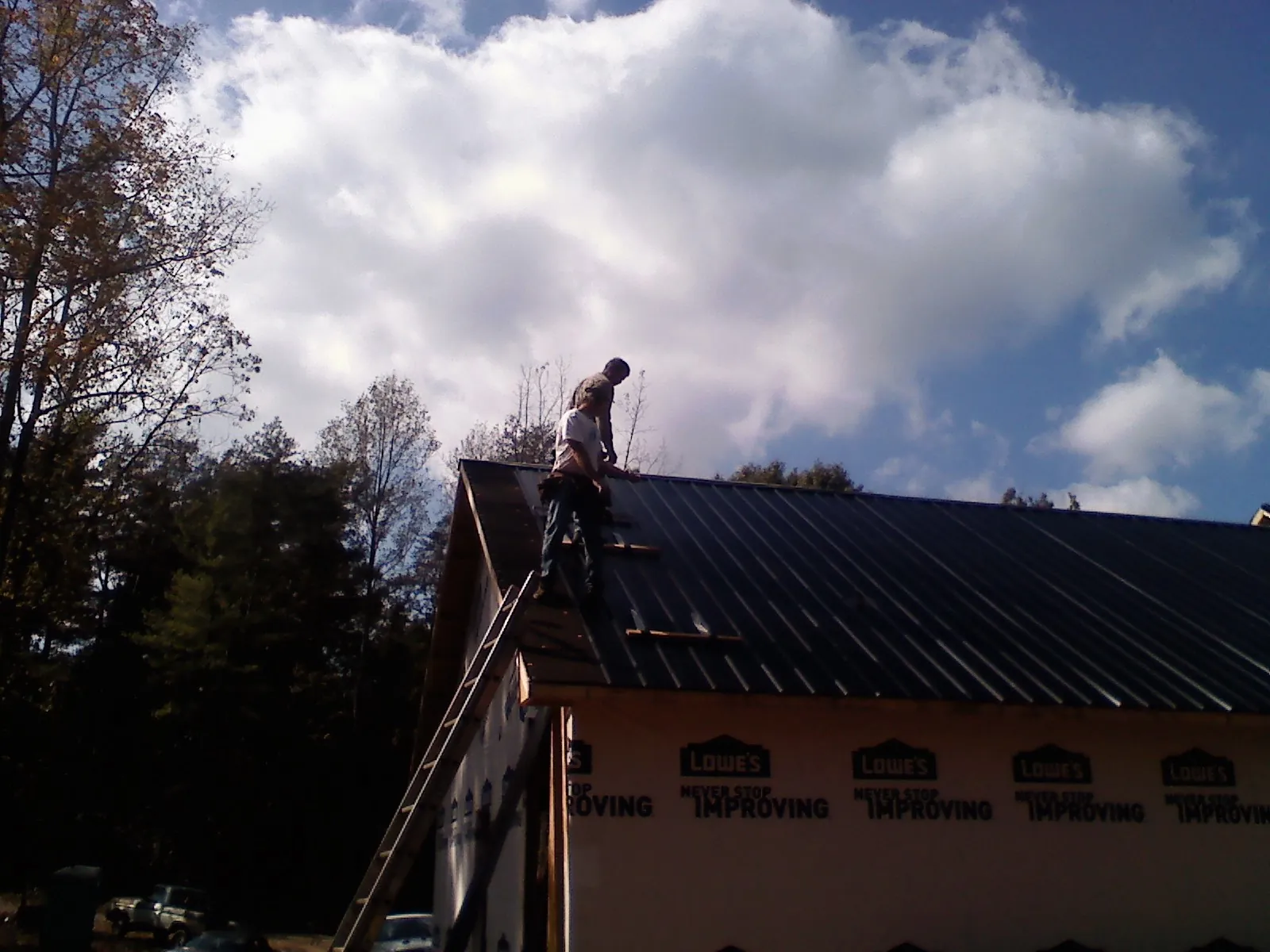 Roofer fastening dark metal panels high against a cloudy sky, from a Roof Inspection job in Walla Walla